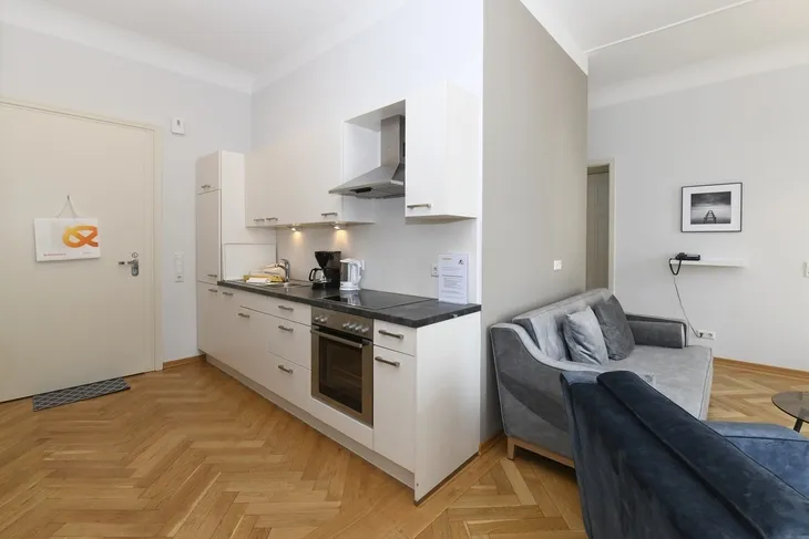 Moderne Küche in einem Wohnraum mit Holzfußboden und grauer Couch.