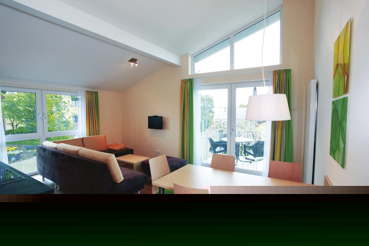 Helles Wohnzimmer mit Essbereich, Sofas, Tisch, großen Fenstern, modernen Möbeln.