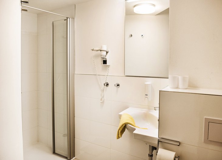 Modernes, helles Badezimmer mit Dusche, Waschbecken und Spiegel.