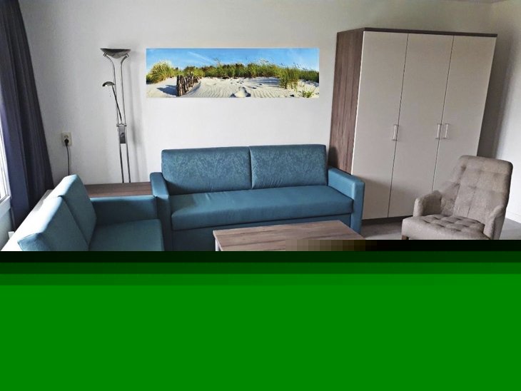 Wohnzimmer einer Ferienanlage mit blauen Sofas, Sessel, Tisch und Schrank.