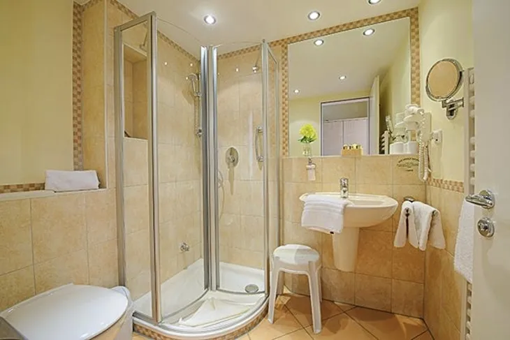 Modernes, helles Badezimmer mit Dusche, Waschbecken, Hocker, Handtüchern und WC, im Haus Oldenburg, in der Ferienanlage Timmendorfer Strand.