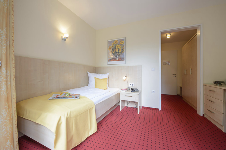Einzelzimmer mit gelber Bettdecke und rotem Teppich in einem Hotel.