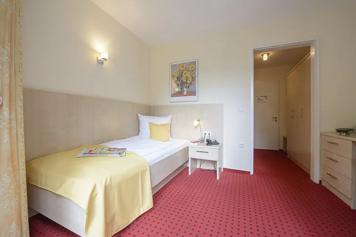 Einzelzimmer mit gelber Bettdecke und rotem Teppich in einem Hotel.
