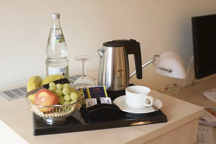 Tablett mit Obst, Wasserflasche, Glas, Wasserkocher und Tasse auf einem Tisch.