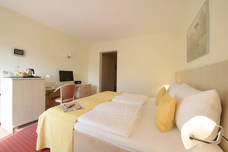 Helles Hotelzimmer mit Doppelbett, Schreibtisch, Fernseher und Wasserkocher.