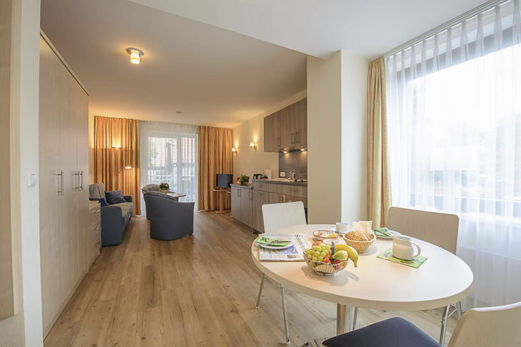 Helles Wohnzimmer mit Esstisch, Sofa und Küchenzeile.
