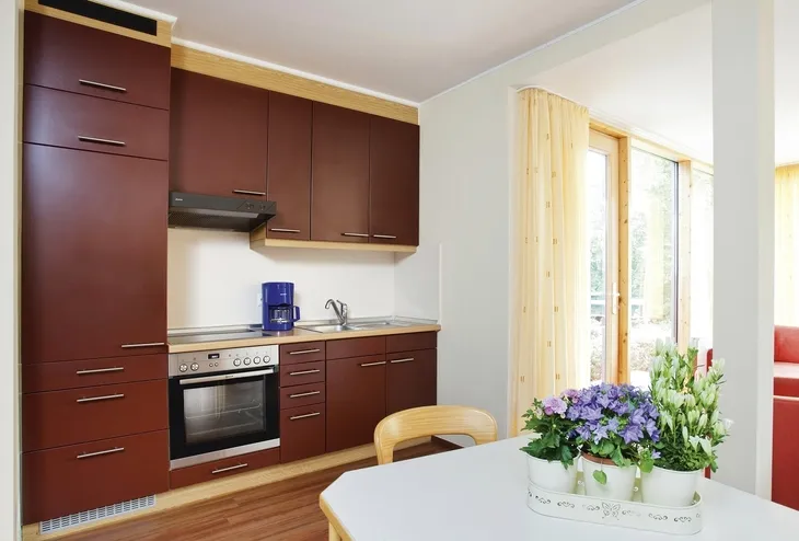 Küche mit roten Schränken, Esstisch und Blumenarrangement in der Ferienanlage Prüm