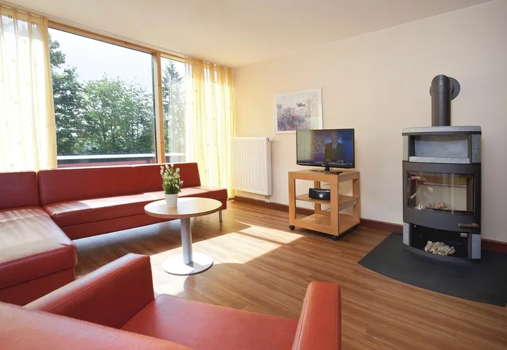 Wohnzimmer mit roten Sofas, einem Kamin und Blick auf Bäume durch große Fenster.