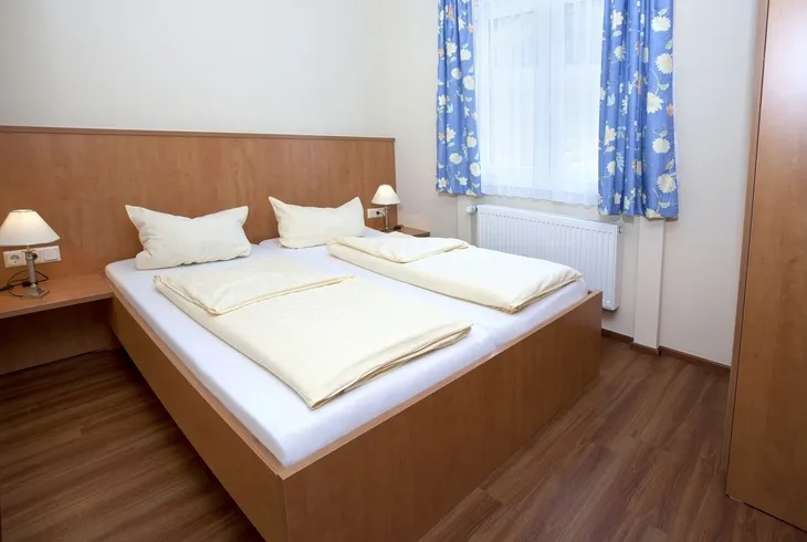 Ein Doppelbett mit Holzmöbeln in einem Zimmer mit blauen Vorhängen in der Ferienanlage Prüm