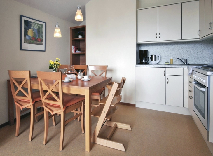Essbereich mit Holztisch, sechs Stühlen, moderner Küche und zwei Hängeleuchten.