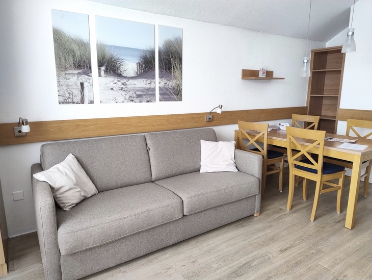 Wohnzimmer mit grauem Sofa, Esstisch und Strandbild an der Wand.