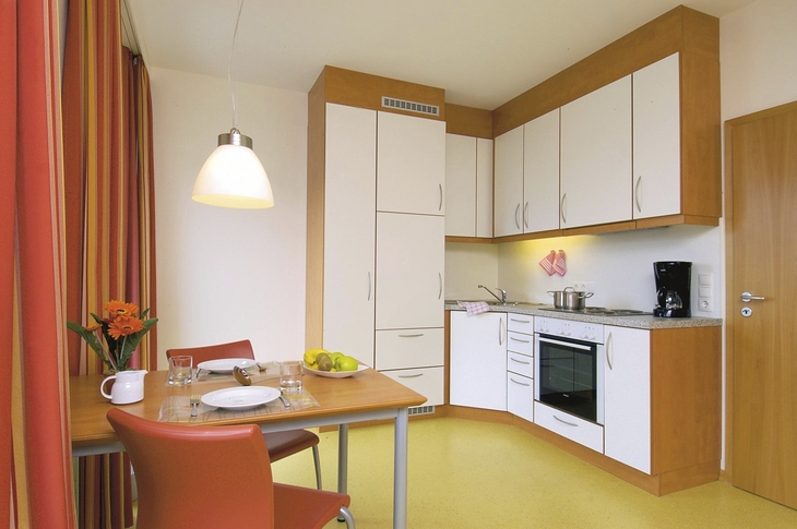 Helle Küche mit Esstisch und Stühlen, sowie langen bunten Vorhängen am Fenster, in der Ferienanlage Wyk auf Föhr.