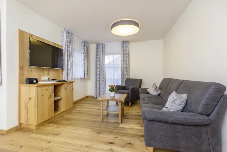 Wohnzimmer mit grauem Sofa, Holztisch und Wandfernseher.