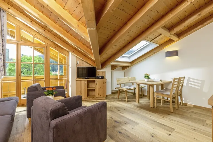Holzverkleidetes Wohnzimmer mit Sitzbereich und Esstisch unter Dachschräge.