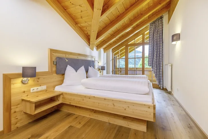 Holzbetontes Schlafzimmer mit Balkendecke und großem Fenster.