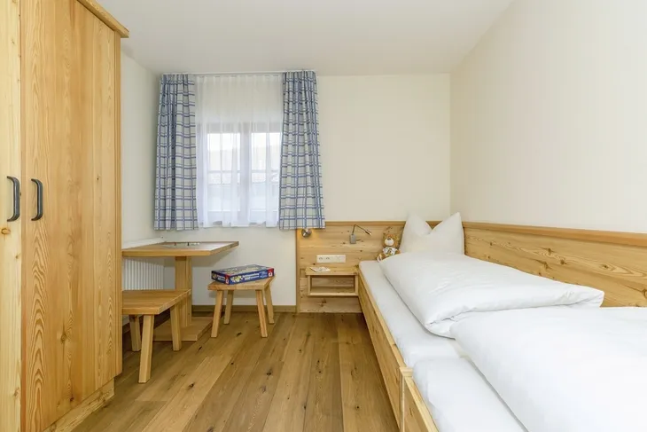 Einzelzimmer mit Holzinterieur und Bett, Schreibtisch, Stuhl und Fenster mit Gardinen.
