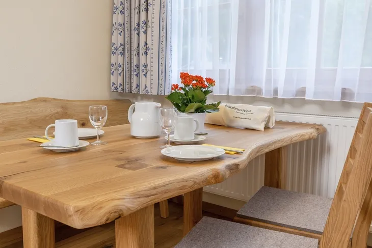 Holztisch mit gedecktem Frühstückstisch, Kaffeekanne, Gläser, Teller und Blumen.