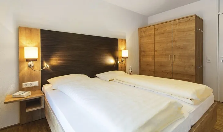 Doppelbett in einem gemütlichen Hotelzimmer mit Holzschrank und Nachttischen