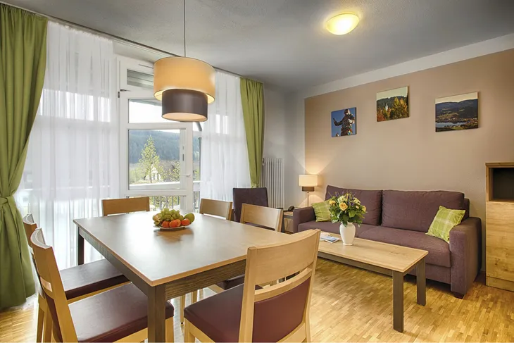 Wohnzimmer mit Esstisch, Sofa, großer Fensterfront und Bildern an der Wand.