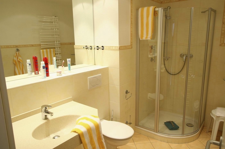 Badezimmer mit Dusche, Waschbecken und gelb-weißen Handtüchern.