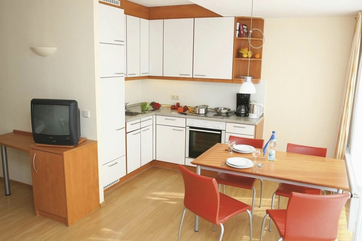 Helle Küche mit Esstisch und Stühlen sowie einem Fernseher im Haus Christel in der Ferienanlage Timmendorfer Strand.