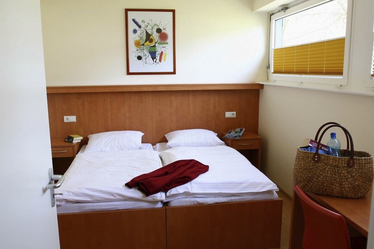 Hotelzimmer mit Doppelbett, Korb auf Stuhl, und Kunstwerk an der Wand.
