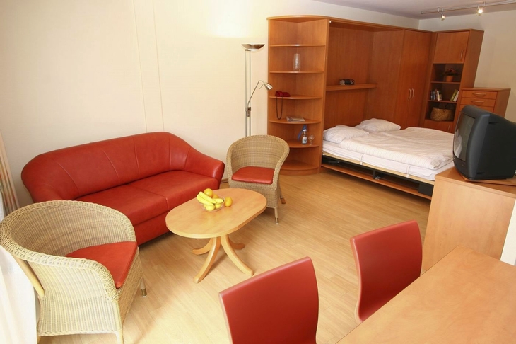 Wohnzimmer mit roten Sitzmöbeln, Holzregal und Fernseher.