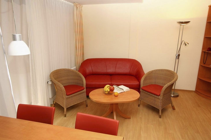 Wohnzimmer mit einem roten Sofa, zwei Korbsesseln und einem runden Holztisch.