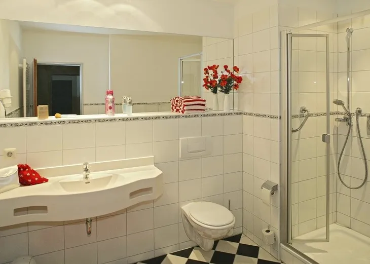 Modernes Badezimmer mit Dusche, Waschbecken und dekorativen roten Blumen.