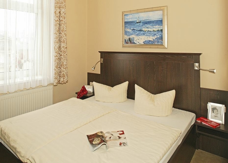 Helles Schlafzimmer mit Doppelbett, Kunst an der Wand und einem offenen Magazin auf dem Bett.
