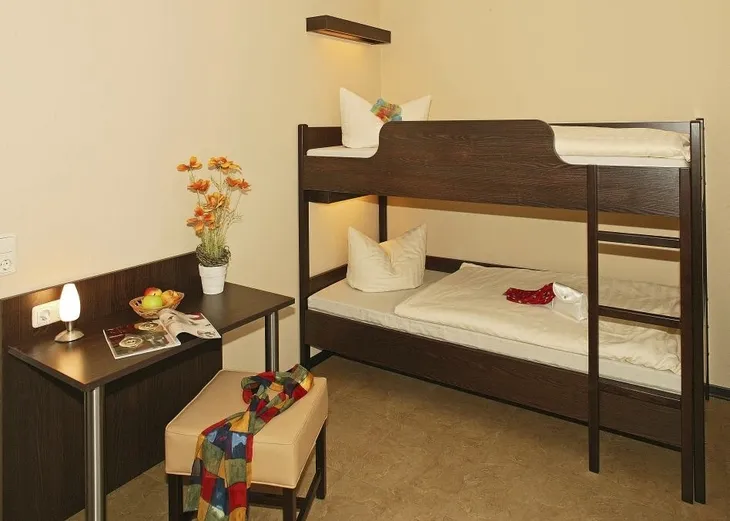 Zimmer mit Etagenbett, kleinem Tisch mit Stuhl, Lampe und Blumendekoration.