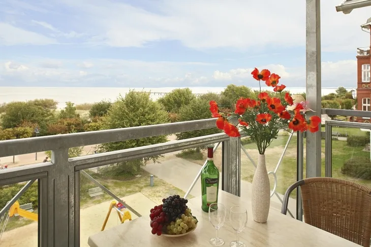 Balkon mit Tisch, Blumenstrauß, Flasche Wein, Gläsern und Blick auf Strand und Meer.