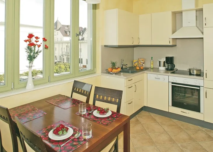 Küche mit Esstisch, hellen Schränken, einem Fenster und Dekoration.
