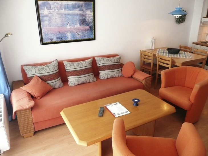 Wohnzimmer mit orangener Sitzecke und Esstisch in einer Ferienwohnung
