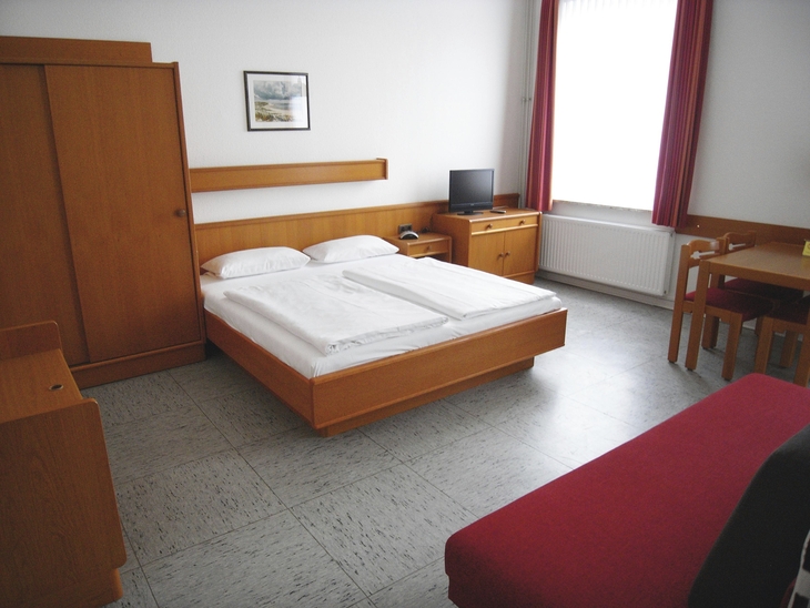 Ein einfach eingerichtetes Hotelzimmer mit Doppelbett und Holzmöbeln.