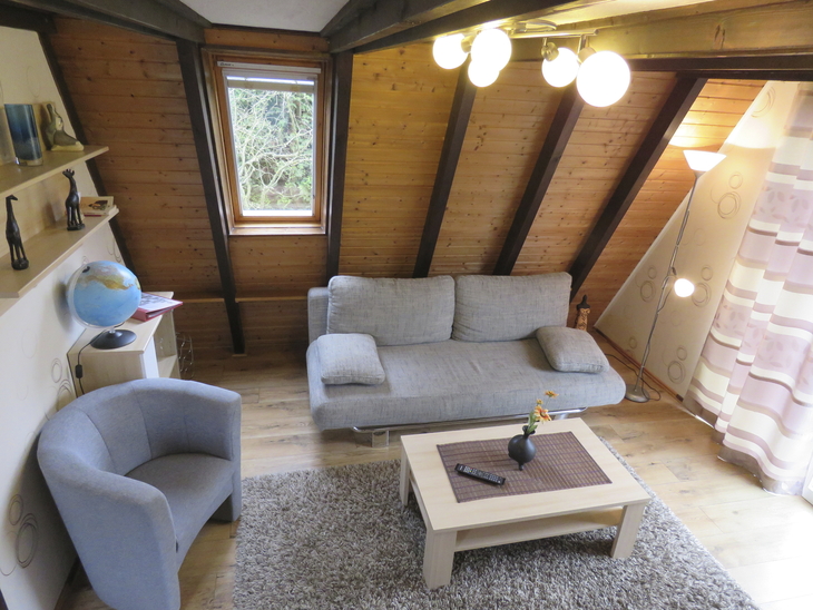 Gemütliches Wohnzimmer mit Sofa, Sessel, Couchtisch und Holzdecke.