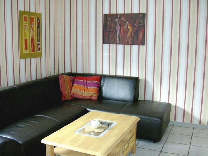 Wohnzimmer mit schwarzem Ledersofa, Holztisch und gestreifter Tapete.
