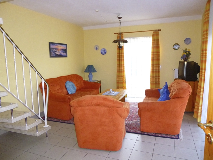 Wohnzimmer mit orangen Sofas, Teppich, Lampe und Treppe im Hintergrund.