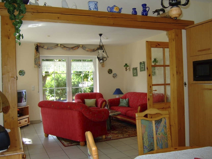Wohn- und Essbereich mit roten Sofas, Tür und Fenster, Tageslicht.