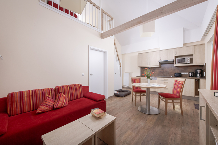 Wohnraum mit rotem Sofa, Esstisch, Küchenzeile und Treppe in Ferienwohnung.