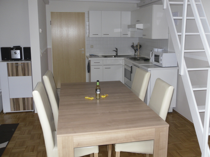 Moderne Küche mit Esstisch, vier Stühlen und Treppe in einer Wohnung.