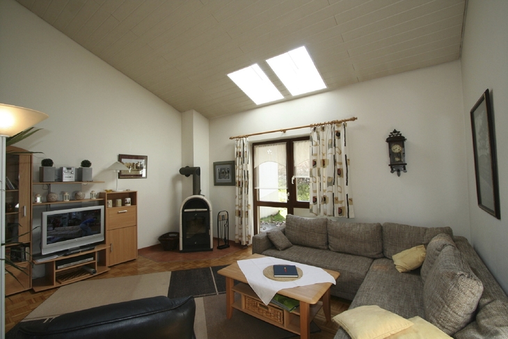 Wohnzimmer mit grauem Ecksofa, Kamin, Fernseher und großem Fenster.