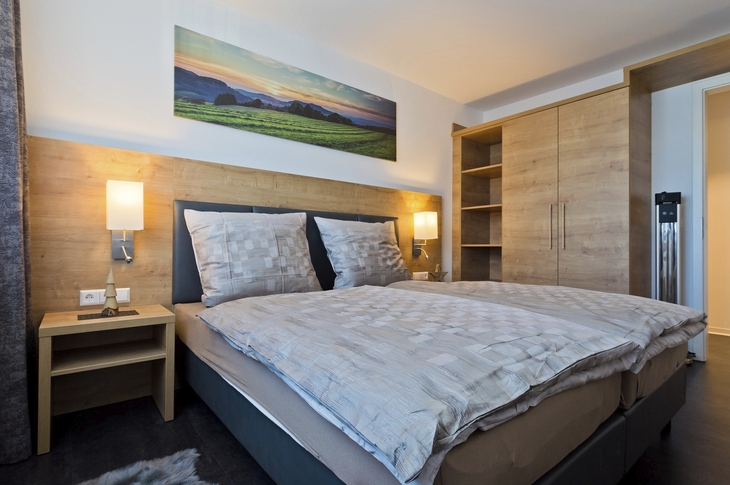 Hotelzimmer mit Doppelbett, Holzdekor, Lampen und Landschaftsbild an der Wand