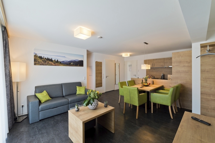 Modernes Wohnzimmer mit grauem Sofa, Esstisch und grünen Stühlen.