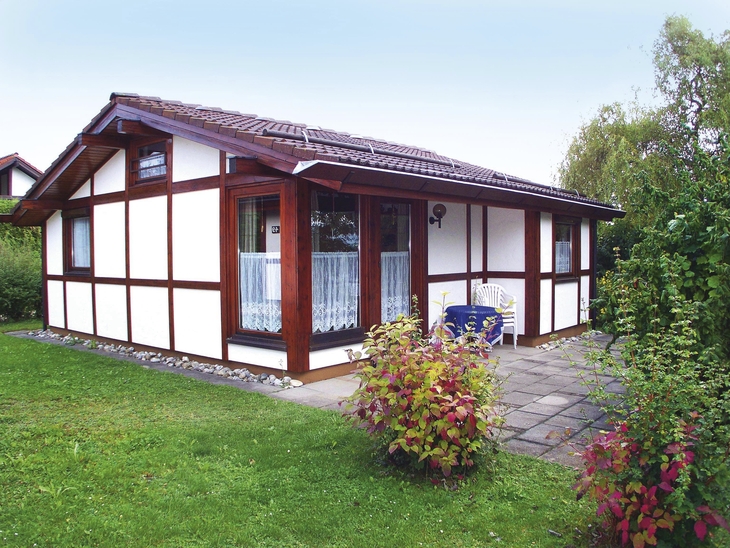 Fachwerkhaus in einer grünen Umgebung mit Terrasse und Gartenmöbeln.