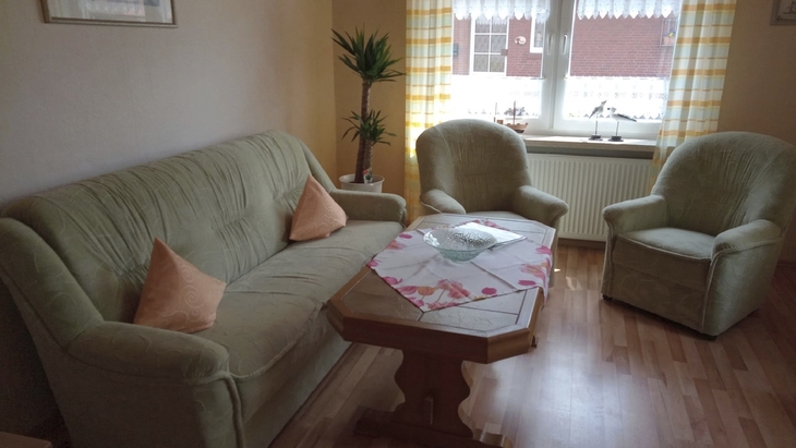 Wohnzimmer mit grauem Sofa, zwei Sesseln, Tisch und großem Fenster.