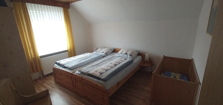 Ein Schlafzimmer mit zwei Betten und einem Beistellbett, Holzboden und gelben Vorhängen.