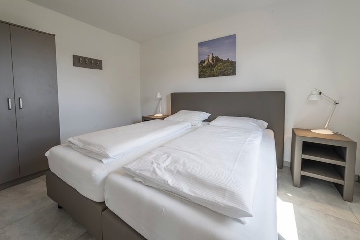Schlafzimmer mit Doppelbett, Schrank, Nachttischen und Wandbild.