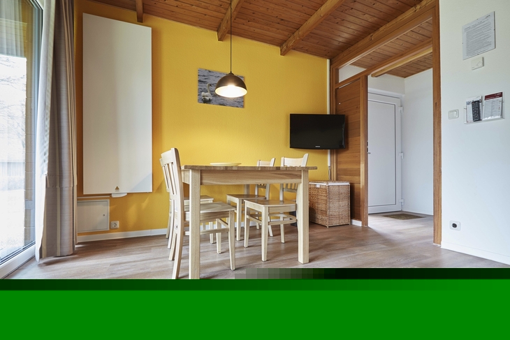 Essbereich in Blockhaus mit Holzmöbeln und gelber Wand, Lampe und Fernseher.