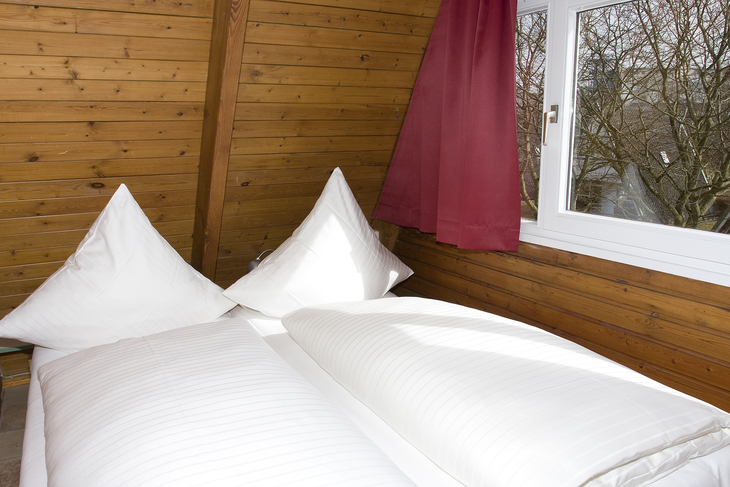 Schlafzimmer mit Doppelbett in einem Nurdachhaus mit Holzverkleidung.